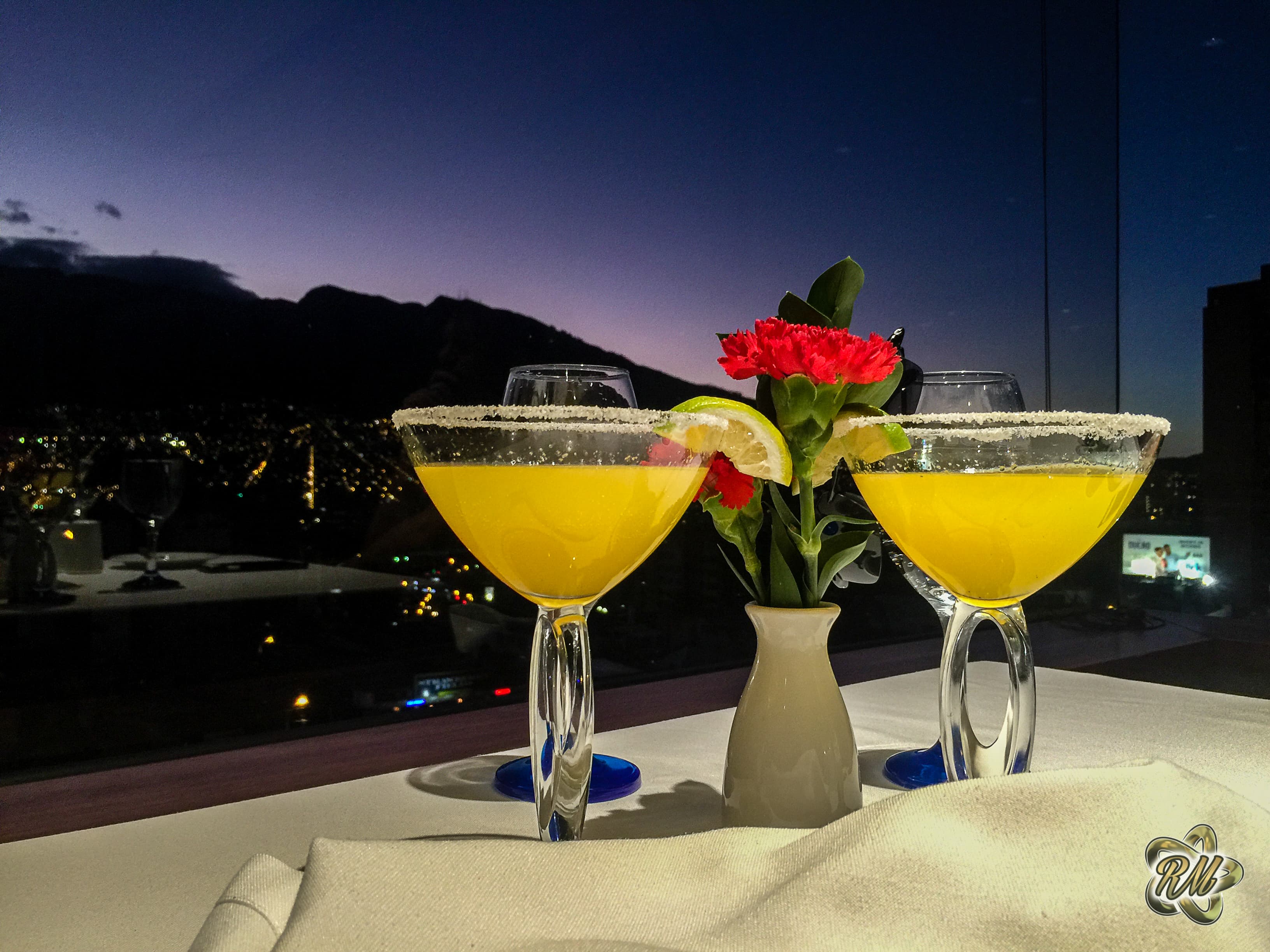 Two cocktails on a wooden surface at sunset, peak silhouette in the distance